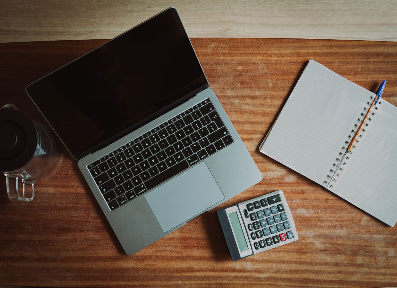 Top view of a desk with a laptop, calculator, and open notepad for work or study.